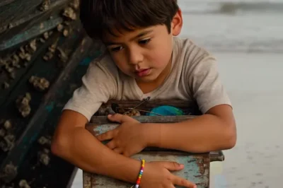 El niño vendía pulseras en el puerto con una sonrisa… pero nadie imaginaba que dormía escondido bajo un bote podrido para no morir de frío